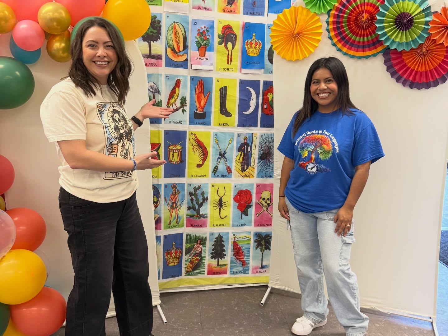 Two Baldy View community members smiling in front of a colorful Lotería event backdrop
